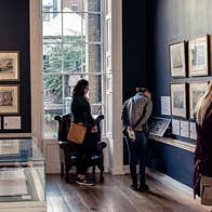 People looking at framed pictures on the wall inside The Little Museum of Dublin