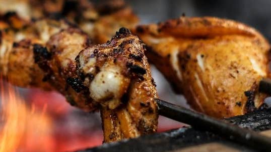 Close up view of meat on skewers cooking over flames.