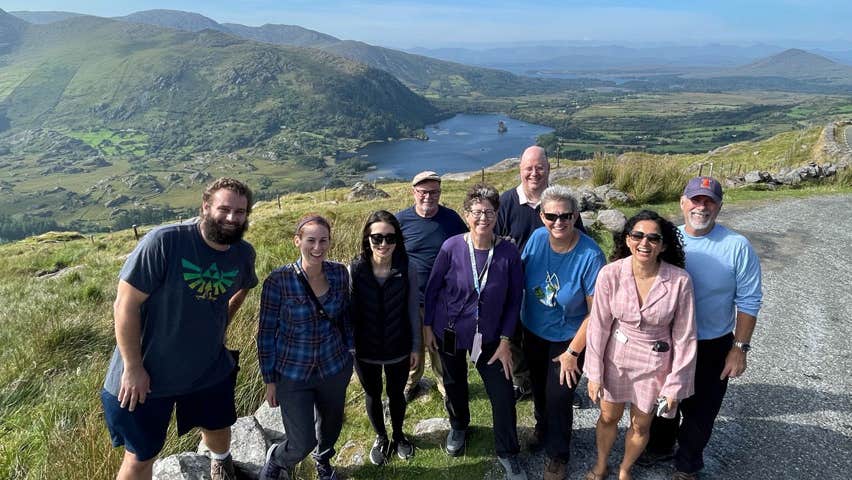 A group of smiling people with hills and the sea in the background