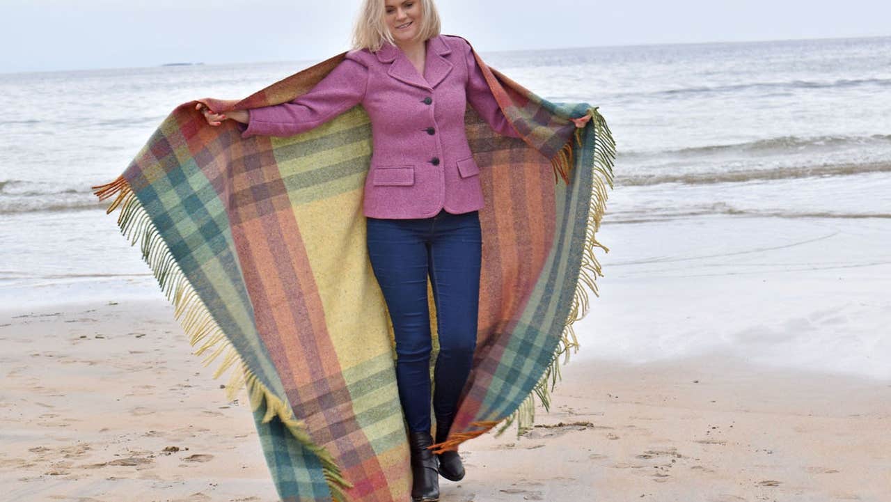 A lady modelling a handwoven throw from Studio Donegal on the beach