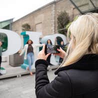 Blonde haired girl holding up a phone to take a photo of her friends at the EPIC sign