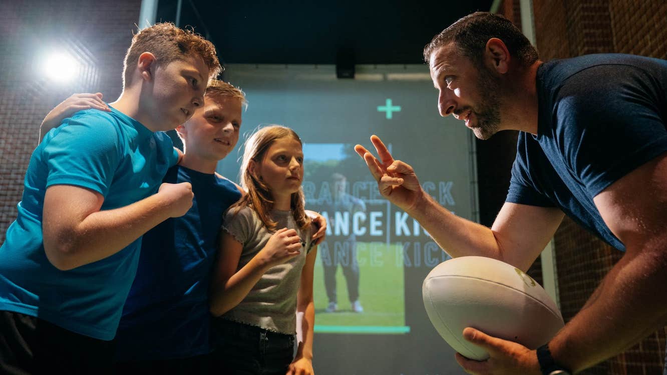 Three children with a staff member holding a rugby ball