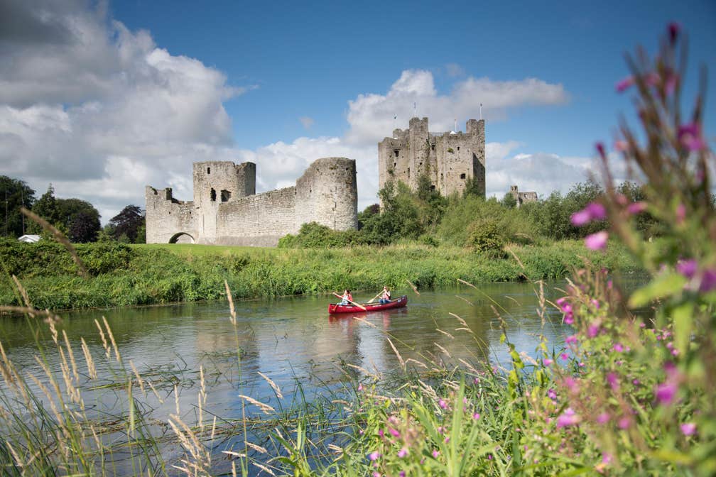 Two people in a rowing boat with views of flowers and Trim Castle nearby