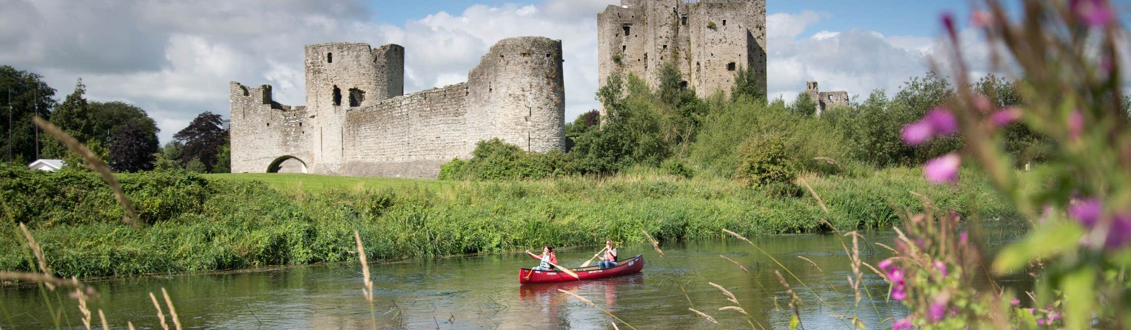 Two people in a rowing boat with views of flowers and Trim Castle nearby
