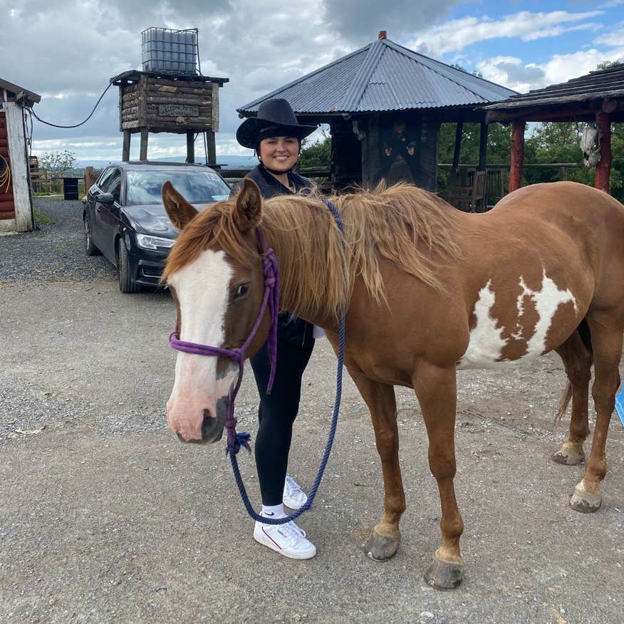 Woman with a cowboy hat on standing beside a brown and white horse.