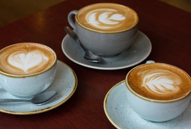 Three cups of coffee on saucers with teaspoons on a table