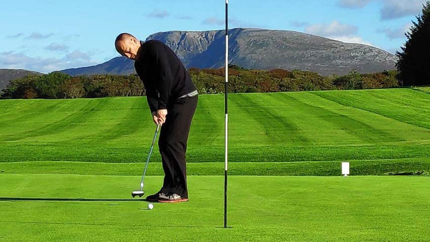 Cloughaneely Golf Club with person putting on a green and Muckish Mountain in the background