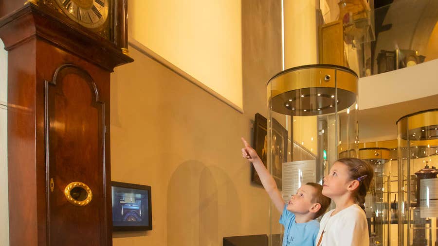 Two children looking up at a grandfather clock with one child is pointing up at it