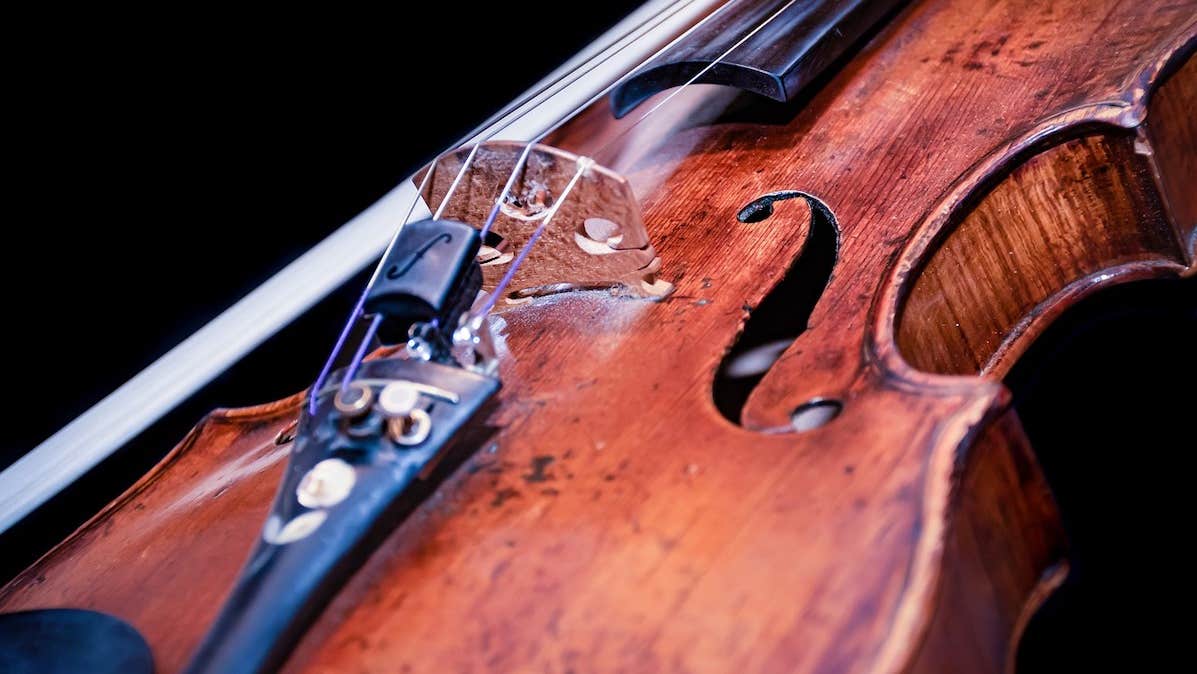 Close up shot of the body of a violin with bow beside it against dark background.