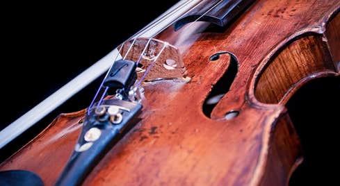Close up shot of the body of a violin with bow beside it against dark background.