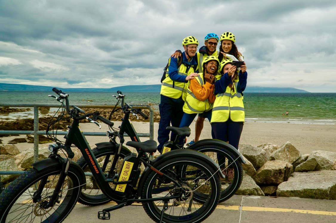 A small group of people posing in front of fat bikes at a beach