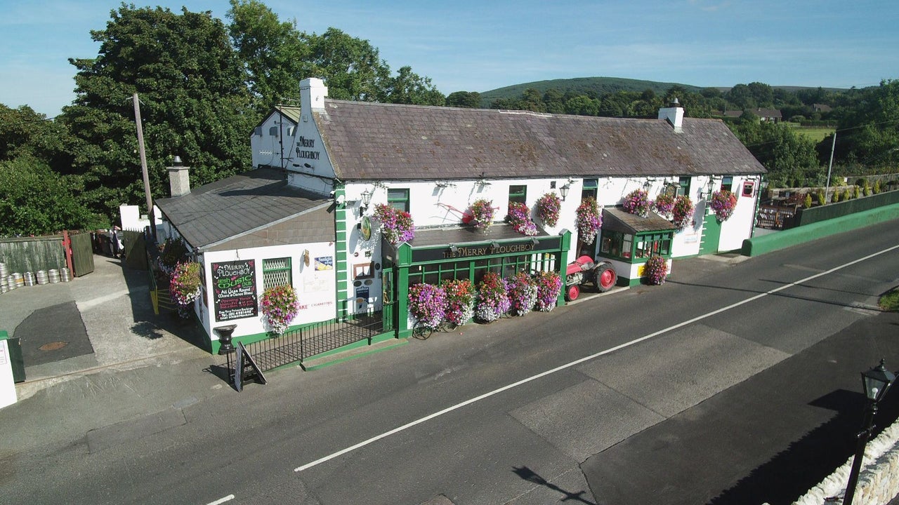The exterior of the Merry Ploughboy Pub which is a white building with green trim and shopfront.