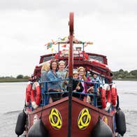 Image of Viking Ship Athlone with people standing at the bow of a small brown ship on the water.