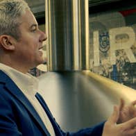 Whiskey expert standing by a nearby still addresses an unseen group of people