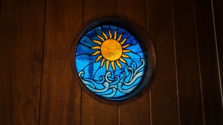 Round stained glass window with sun and wave design set into a wooden sauna wall