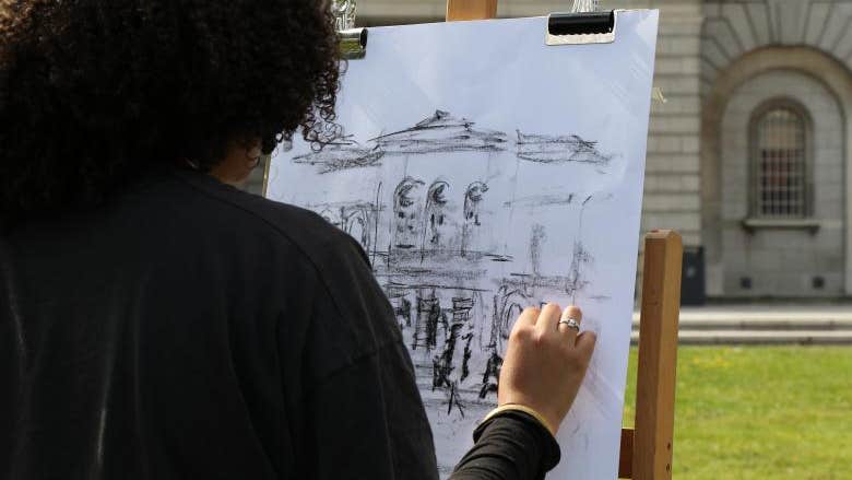 Rear view of person drawing on easel outdoors in front of a building