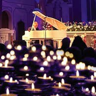 In the distance a man playing a white grand piano with lots of blurry candles in the foreground.