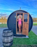 Lady in a pink swimsuit standing in the doorway of an open sauna by a lake