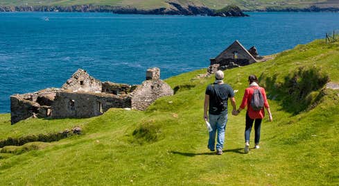 Two hikers walking on a grassy trail near abandoned buildings on Blasket Islands, Kerry.