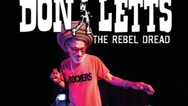 A man in T-shirt and large hat is standing behind a record mixing deck