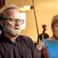 A seated man is singing with his eyes closed