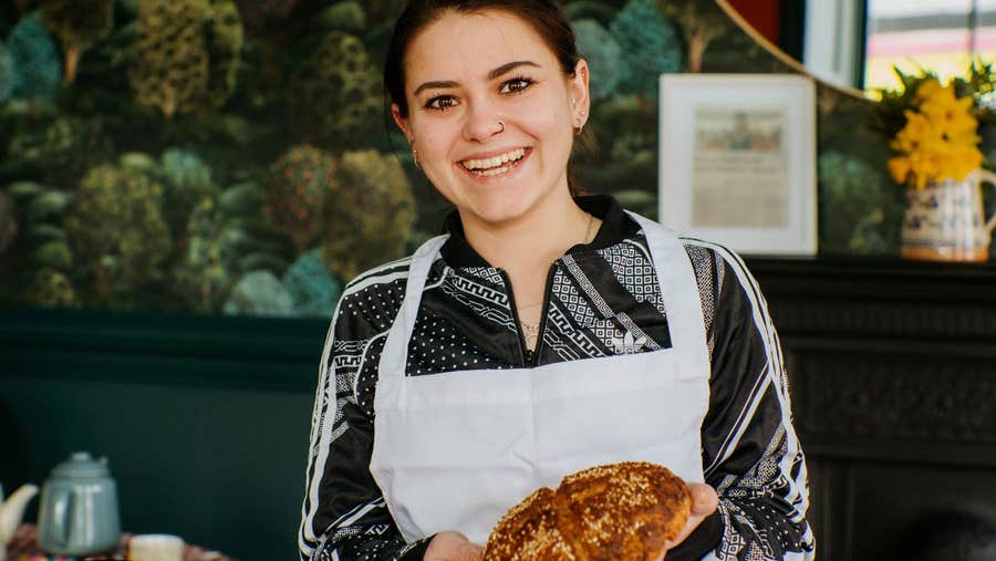 A lady in an apron holding an Irish soda bread scone