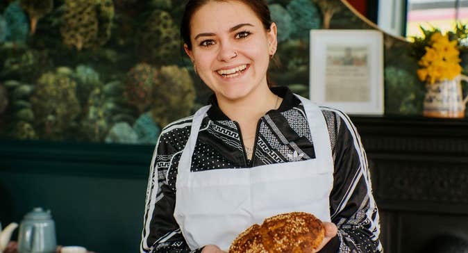 A lady in an apron holding an Irish soda bread scone
