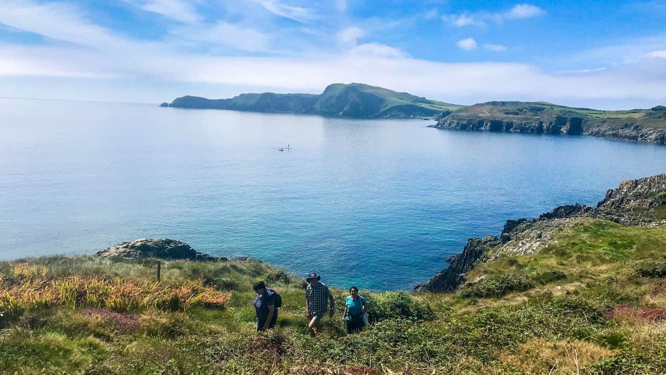 Three people on a walking trail with a view of the West Cork coastline in the background