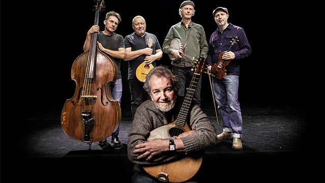 A group of 4 men holding instruments with another crouched down in front hugging a musical instrument.