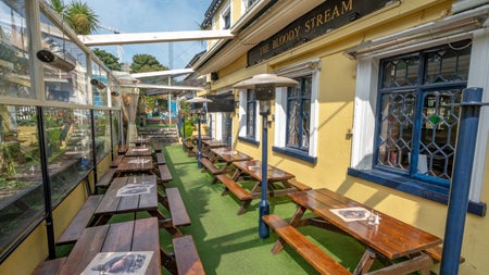 Two rows of brown picnic benches outside a yellow pub