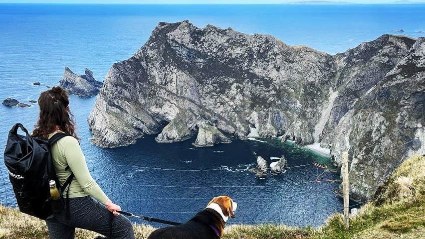 A woman with two dogs looking down at the Slieve League Cliffs