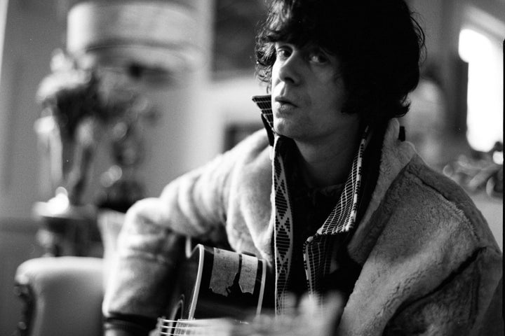 Photo in black and white of man playing a guitar with background blurred.