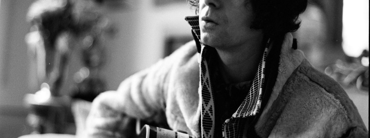 Photo in black and white of man playing a guitar with background blurred.