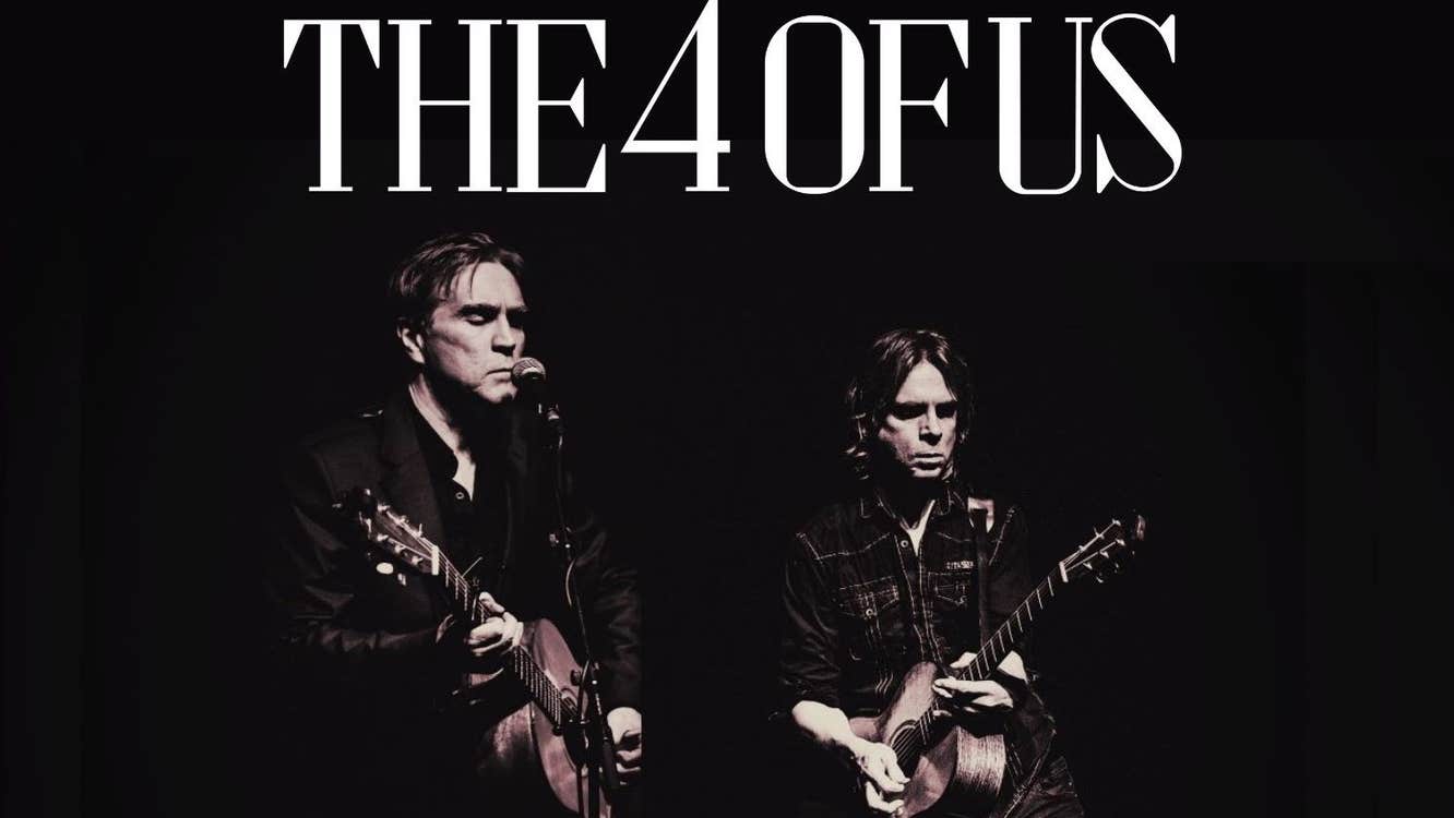 2 men playing guitars in dark clothes against black background.