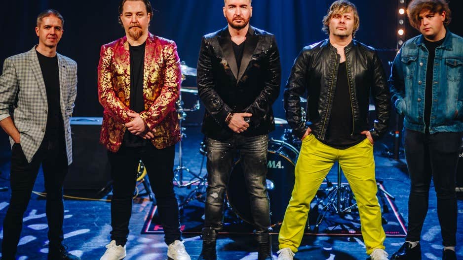 A line of 5 men in bright or shiny black jacket on the front of a stage.
