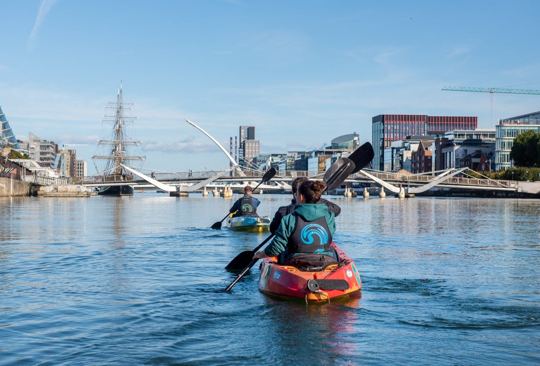 Two kayaks with three people paddle on the River Liffey towards the Samuel Beckett Bridge