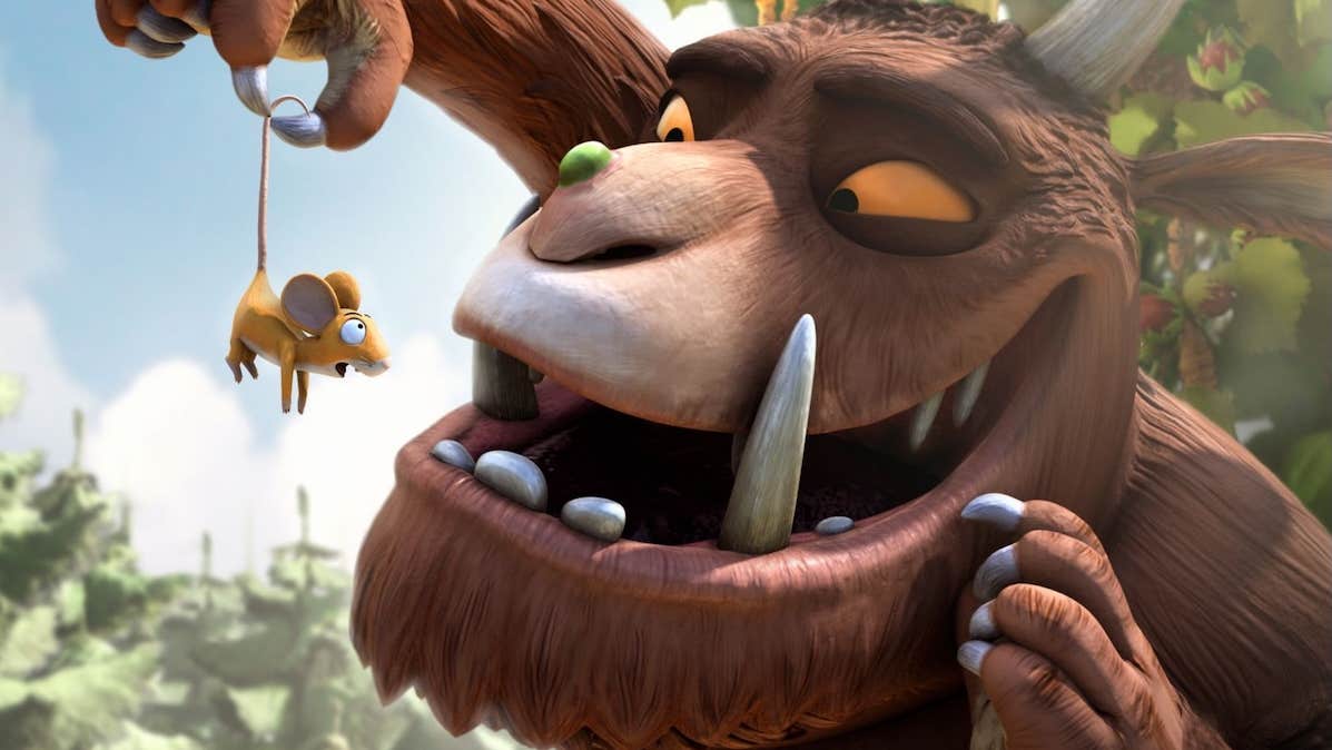 A large brown animal with tusks is holding up a tiny shocked mouse in front of his face