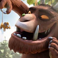 A large brown animal with tusks is holding up a tiny shocked mouse in front of his face
