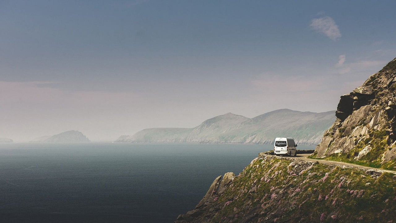 A bus with a logo parked along a cliff road with a dramatic coastal view
