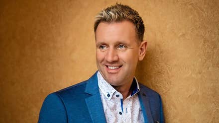 Mike Denver - a smiling man looking away to his right against dark gold background.