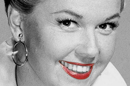 Black, white, grey close up face picture of Doris Day smiling at the camera, with bright red lipstick.