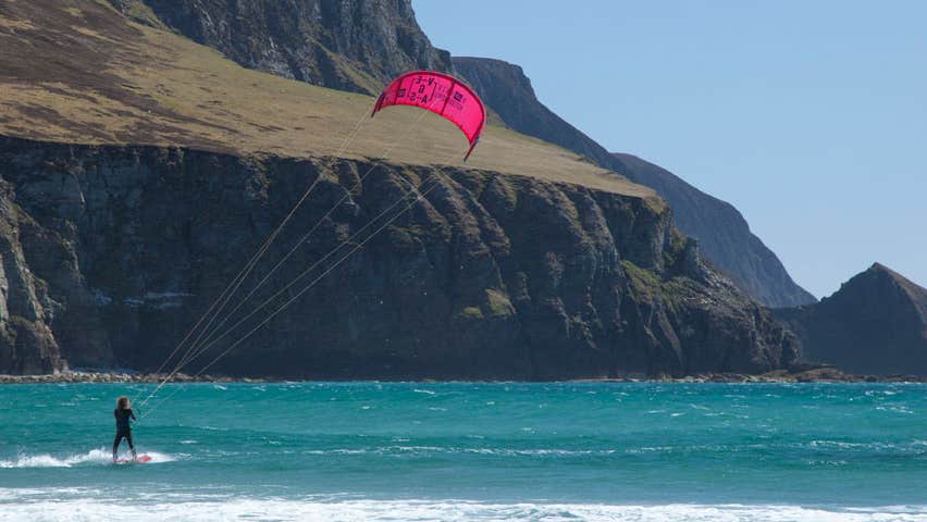 A person kitesurfing at the foot of high cliffs