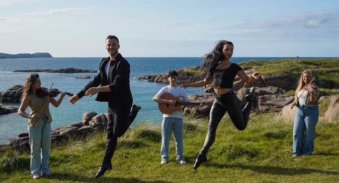 5 people standing with instruments or leaping in the air, outdoors on a rocky edge overlooking the sea.
