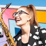 Jess Gillam holding her saxophone in front of a colourfully painted wall