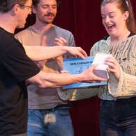 A man presenting a small box and certificate to a surprised looking woman.