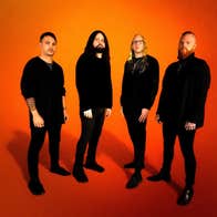 Illinois progressive metal band Born of Osiris, 4 serious looking men dressed all in black, against plain orange background.