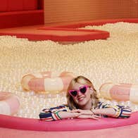 Person wearing pink heart shaped sunglasses in a full ball pit with three inflatable lifebuoys