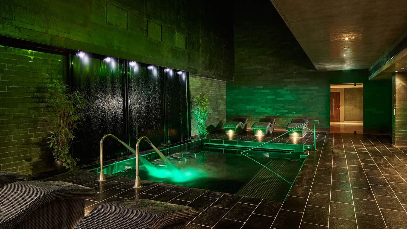 A wall to floor tiled room with a small pool