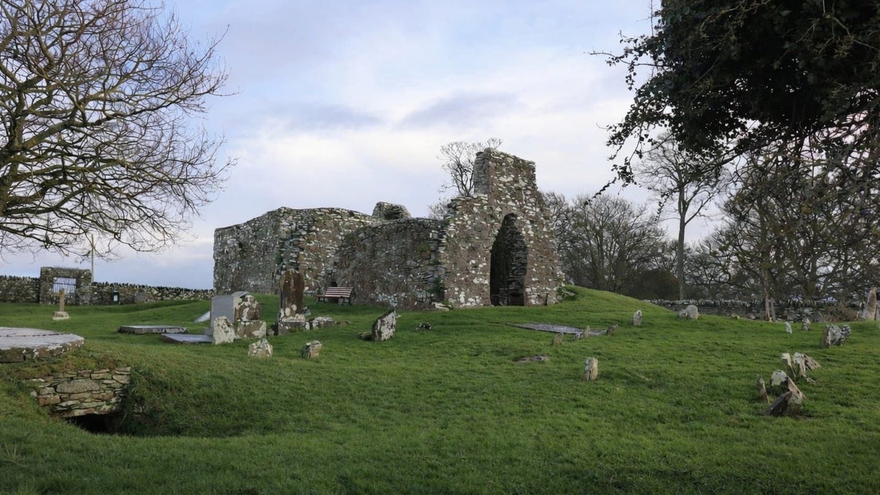 Ruins of an old stone church surrounded by scattered gravestones on a grassy hillside