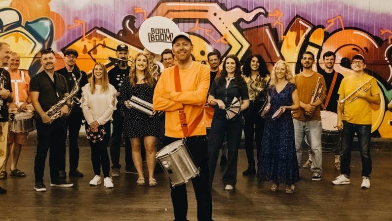 A large group of smiling people, most holding musical instruments.